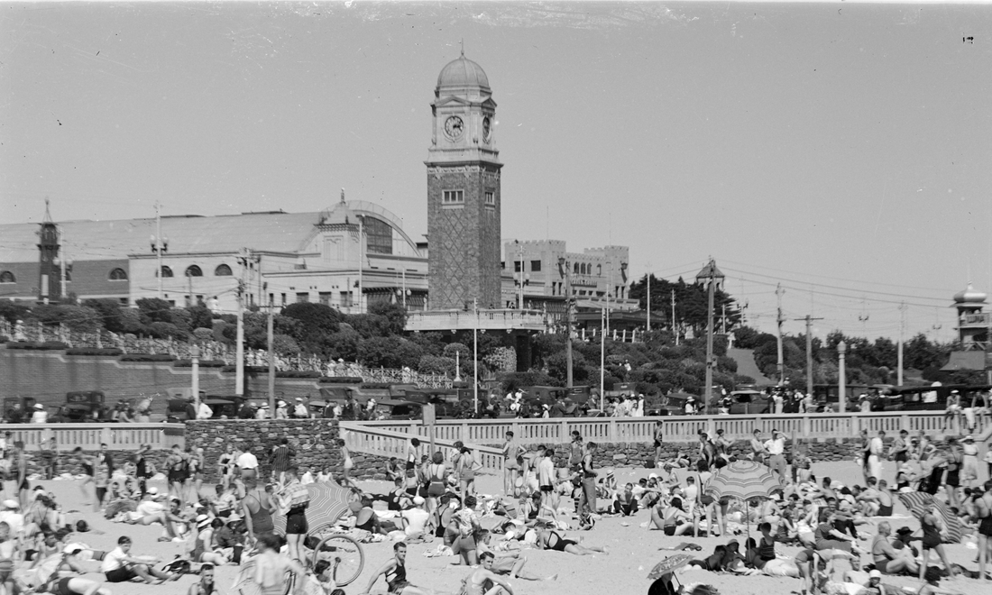 Crowded St Kilda Beach in Melbourne during the 1940s with the St Kilda Sea Baths clock tower overlooking beachgoers.