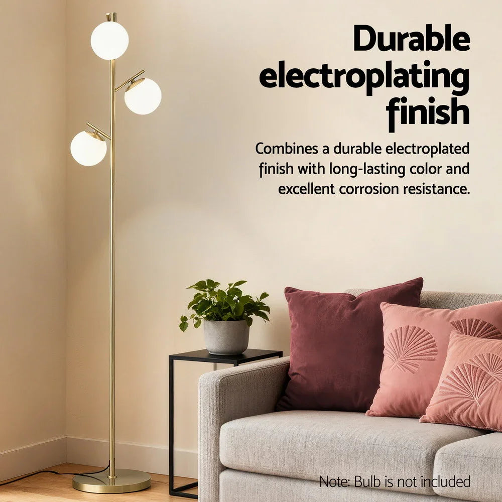 Modern gold floor lamp with three frosted globe lights next to sofa in cozy living room corner.