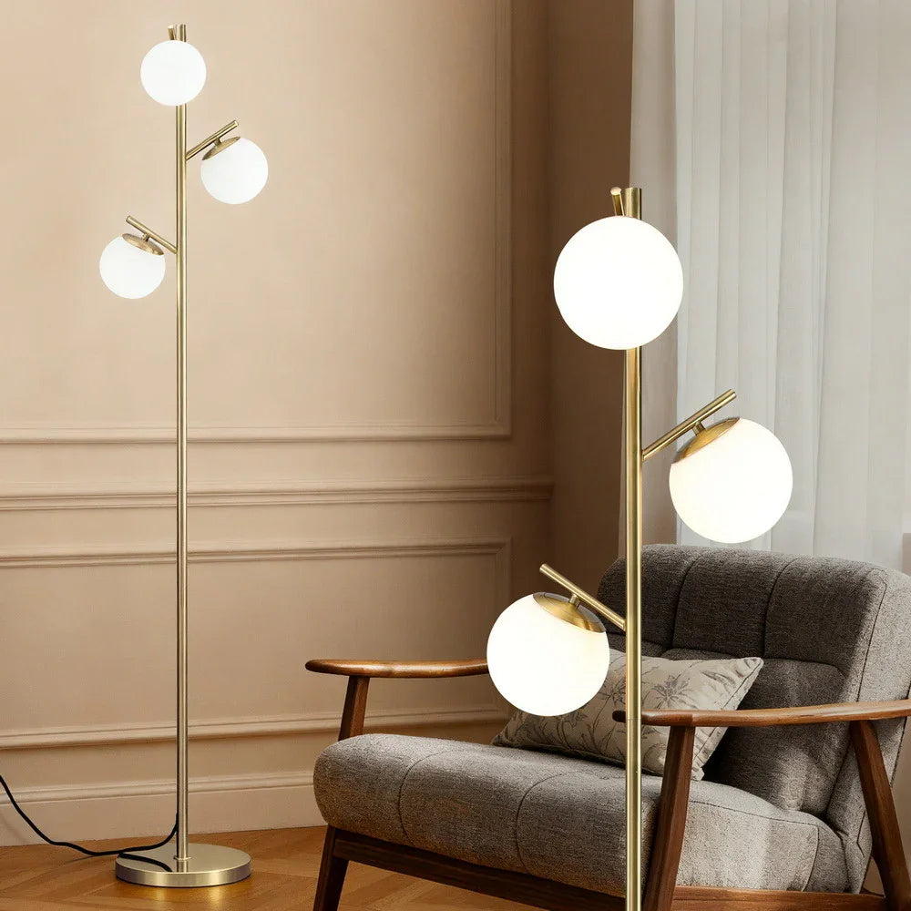 Modern gold floor lamp with three glass globe lights in a cozy living room setting