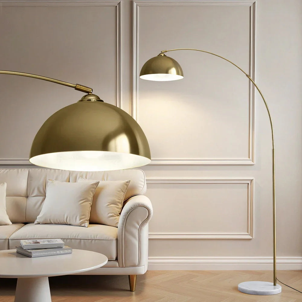 Modern gold arc floor lamp with dome shade in elegant living room beside beige sofa