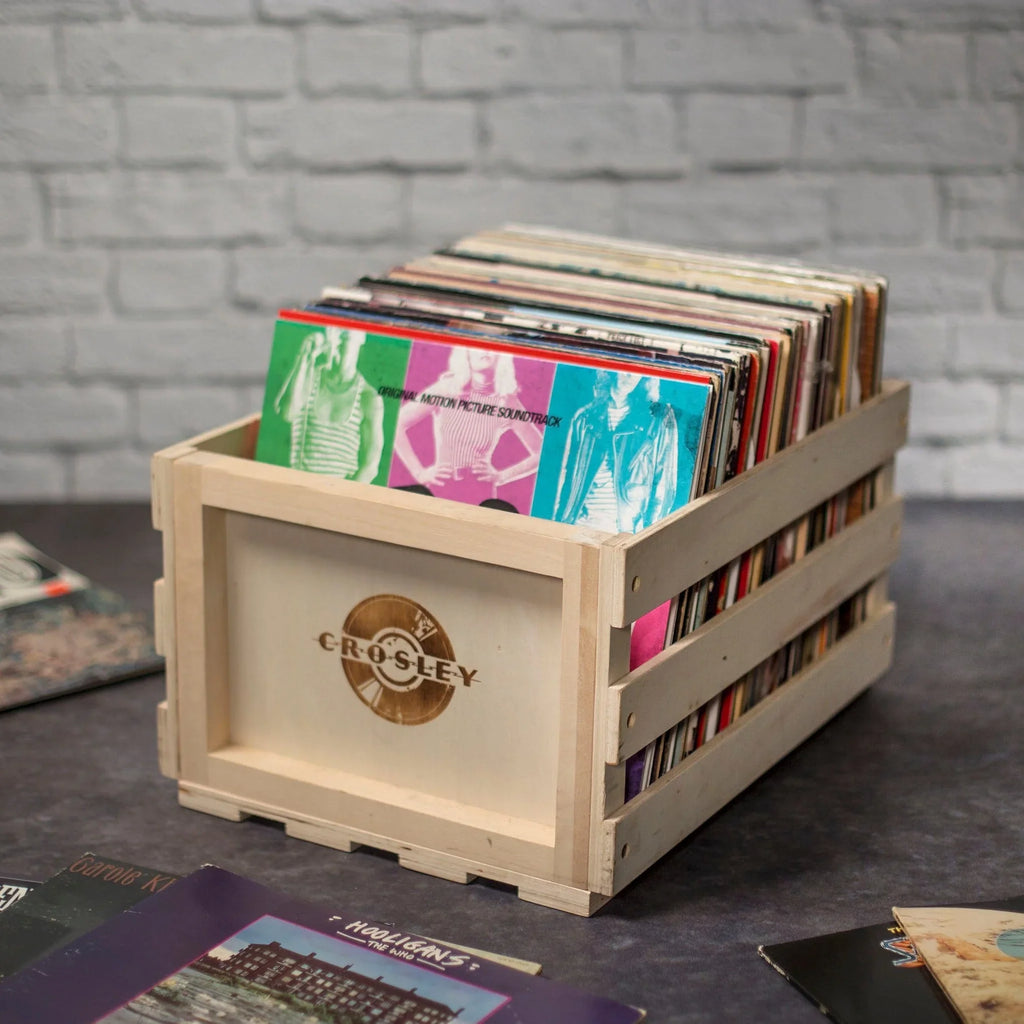 Wooden Crosley record crate filled with vinyl records on a dark tabletop, brick wall background.