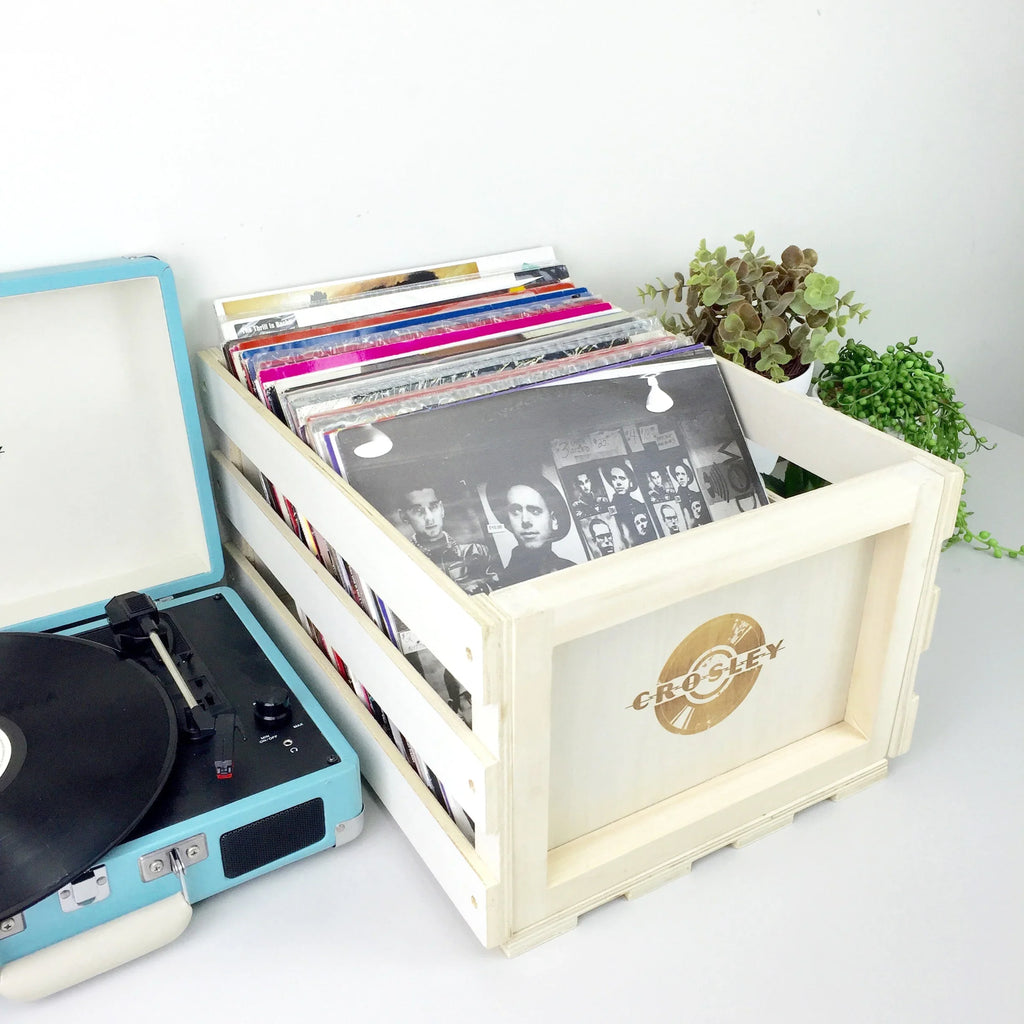 Crosley wooden record crate with vinyl albums beside a blue portable turntable and plants