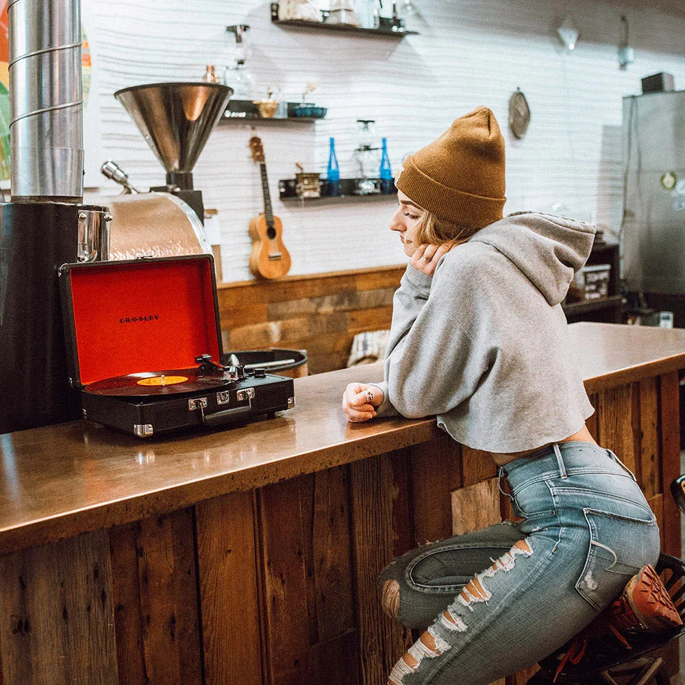 Woman in a beanie and ripped jeans sitting at a rustic counter with a Crosley record player
