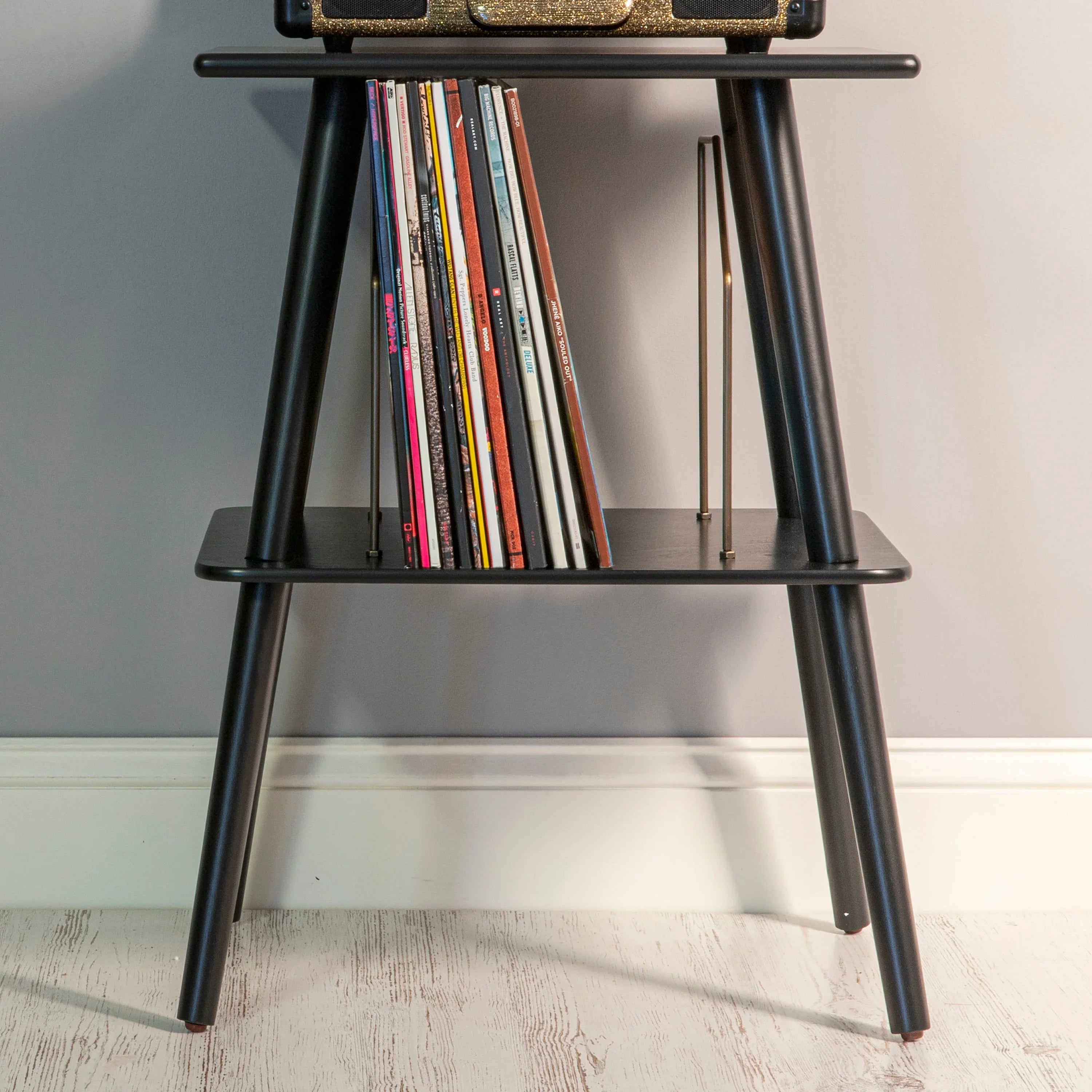 Black wooden record player stand holding vinyl records against a gray wall