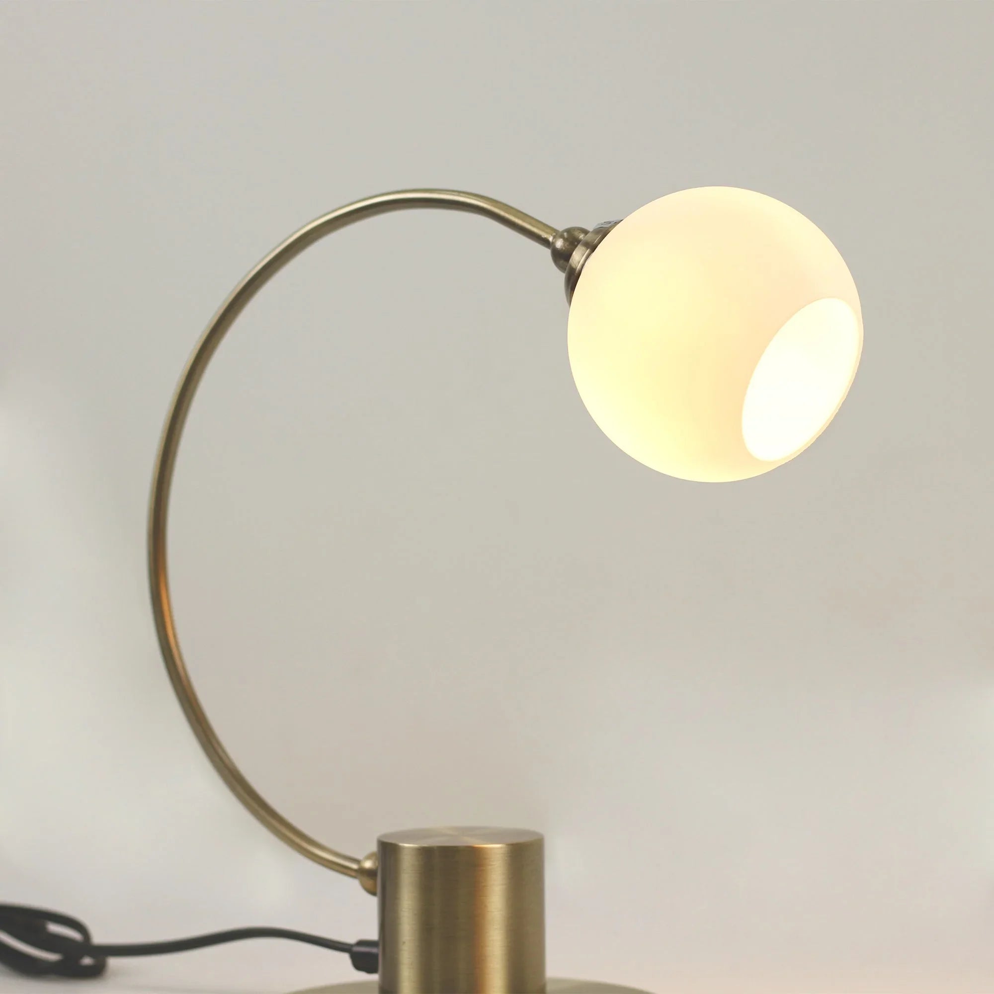 Modern brass table lamp with curved arm and frosted glass globe shade
