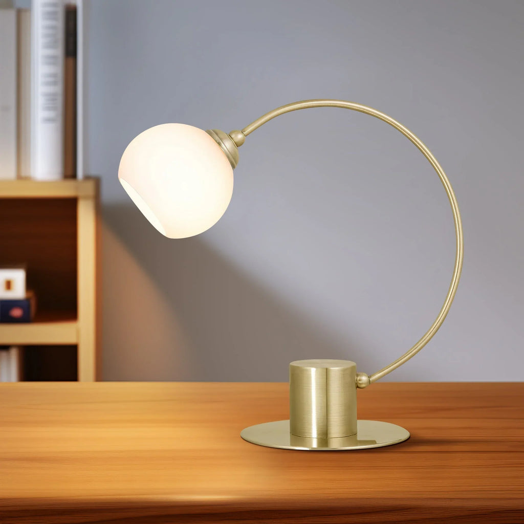 Modern brass desk lamp with round white glass shade on wooden table in minimal office