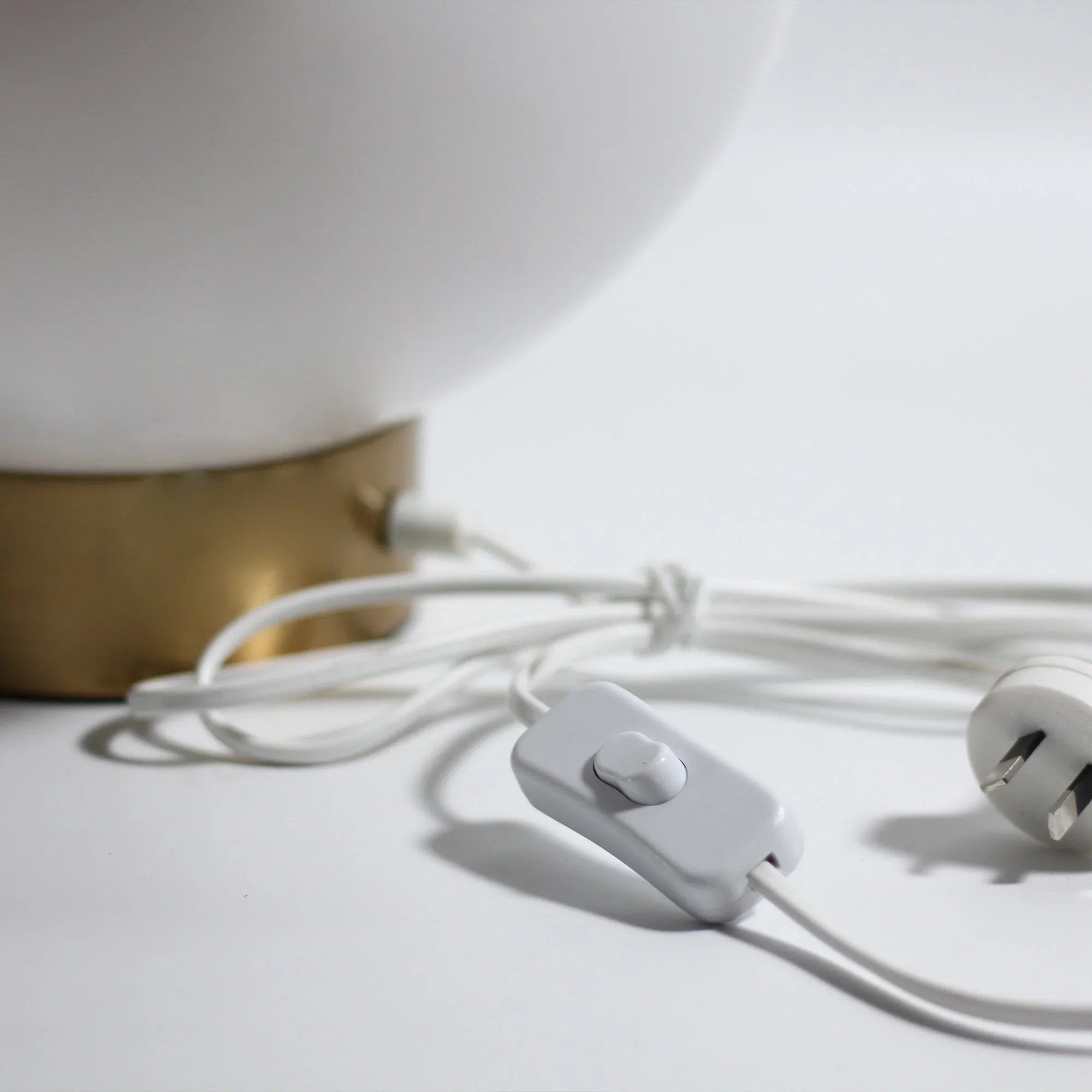 Close-up of table lamp base with gold accent, white cord, and switch plug